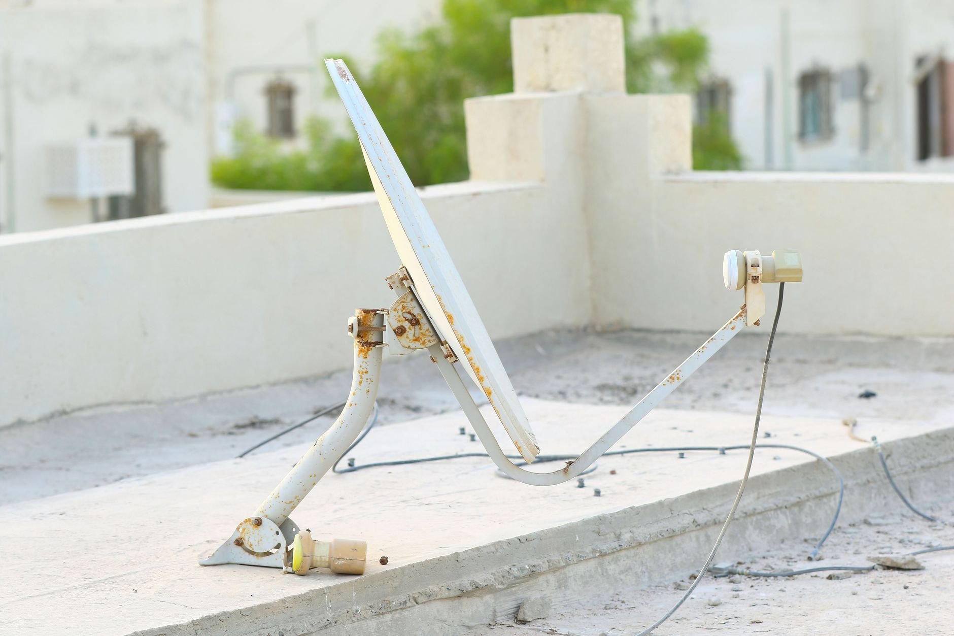 Weathered white satellite dish with a bracket arm and a small LNB on a flat concrete rooftop