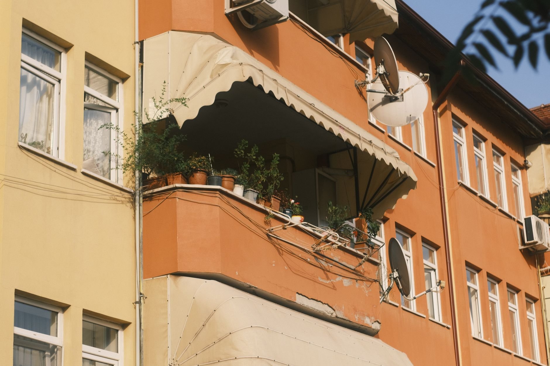 Orange apartment building facade with several satellite dishes mounted on balconies and walls