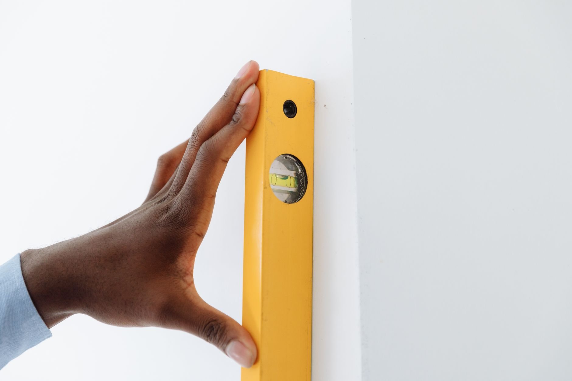 Hand holding a yellow spirit level with a bubble vial against a white wall