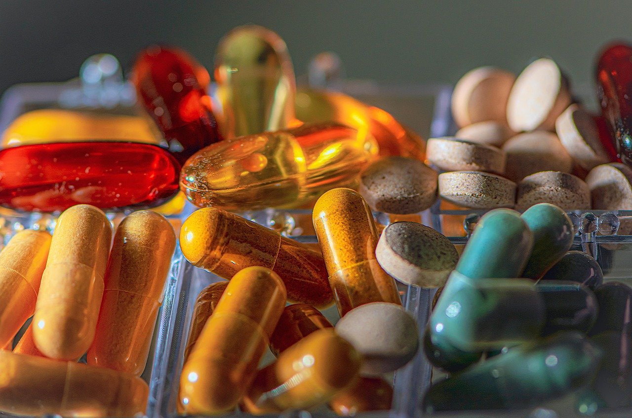Assorted capsules and tablets in red, orange, yellow, teal, and cream colors, arranged in a clear tray.