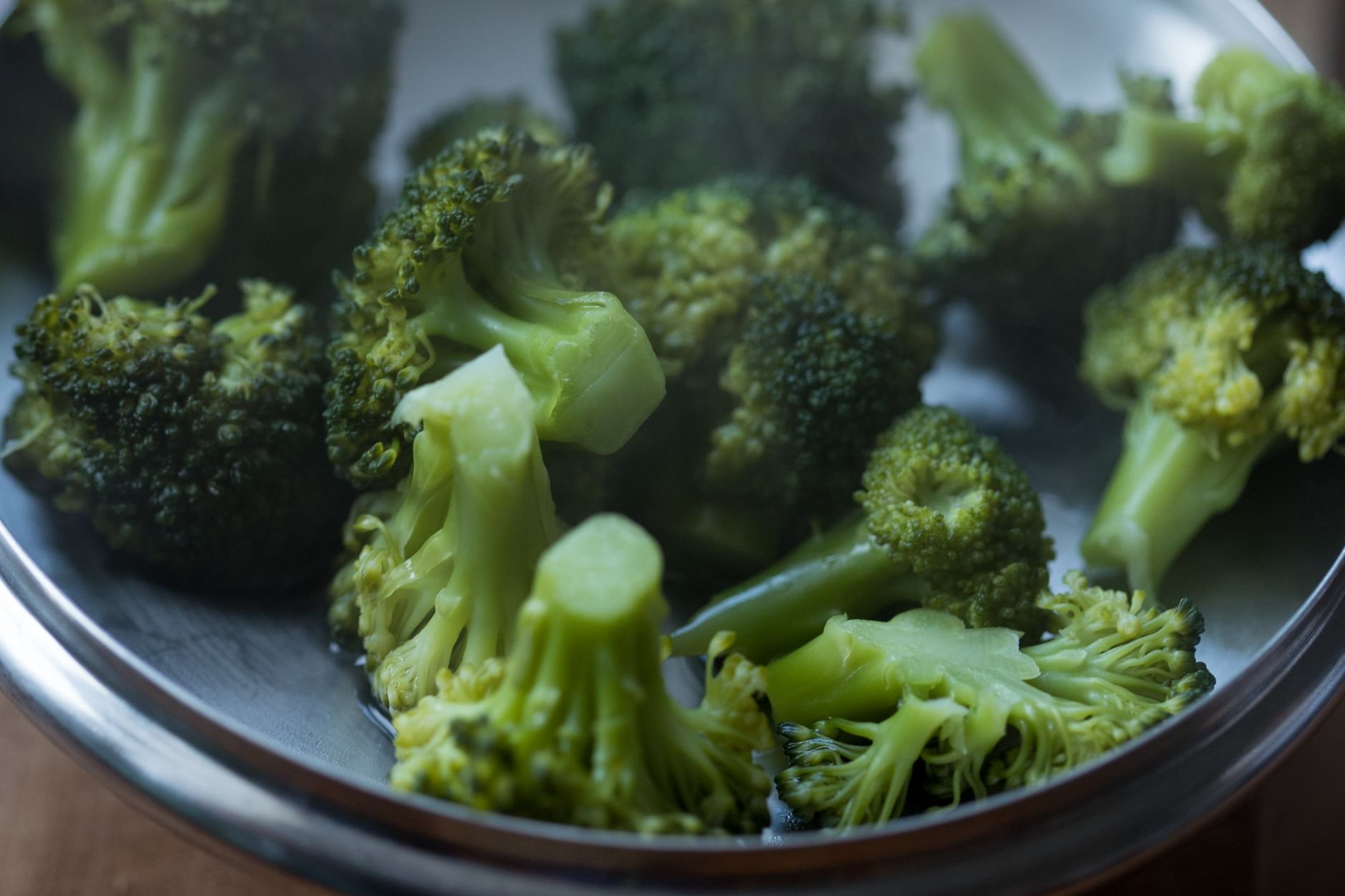 Bright green broccoli florets in a metal bowl with water droplets on the surface