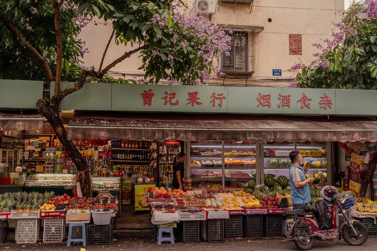 Street-level produce shop with a green fascia sign in Chinese characters and fruit displayed on the sidewalk