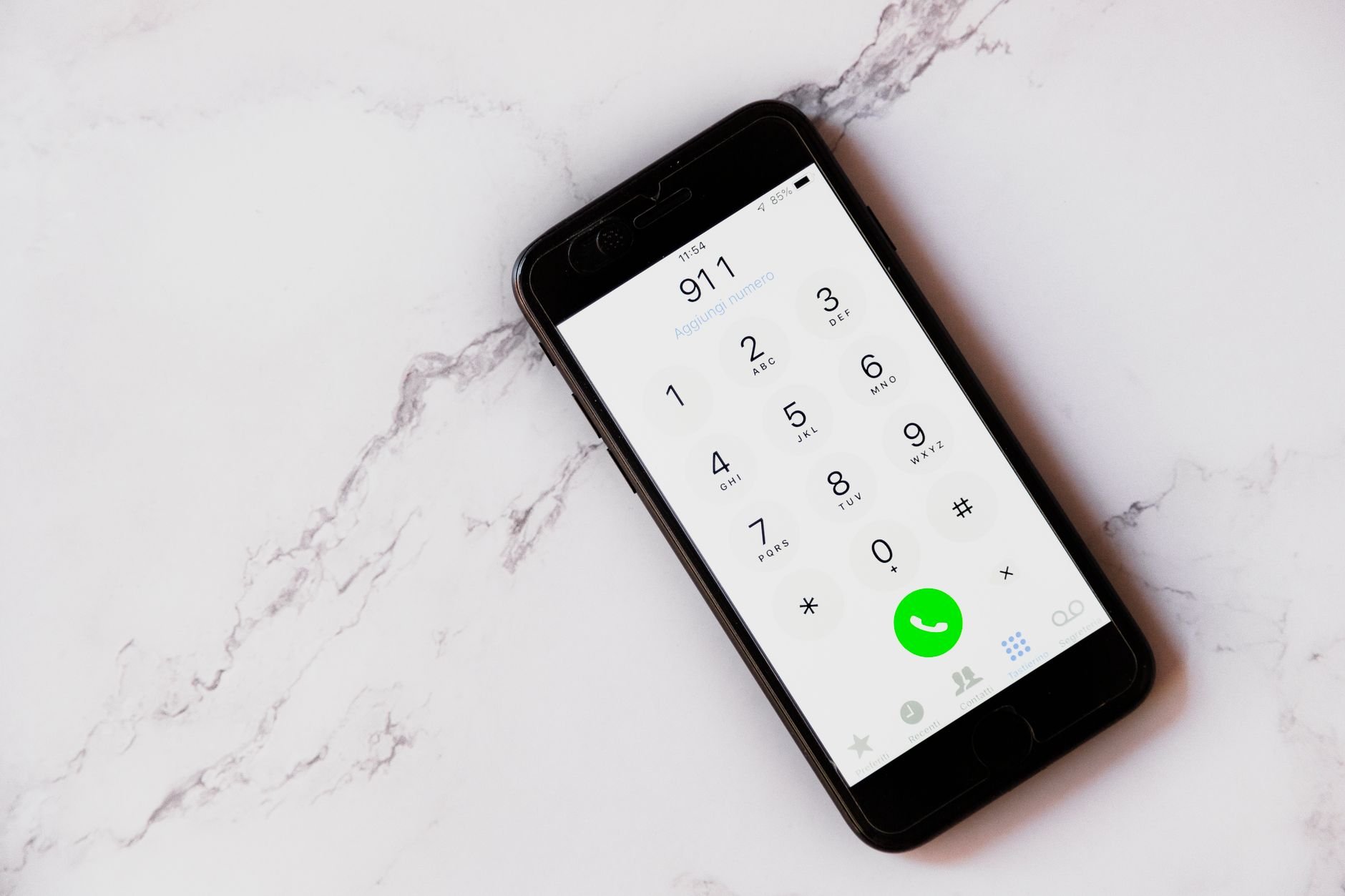 Black smartphone on a white marble surface showing a dialer with 911 entered and a green call button