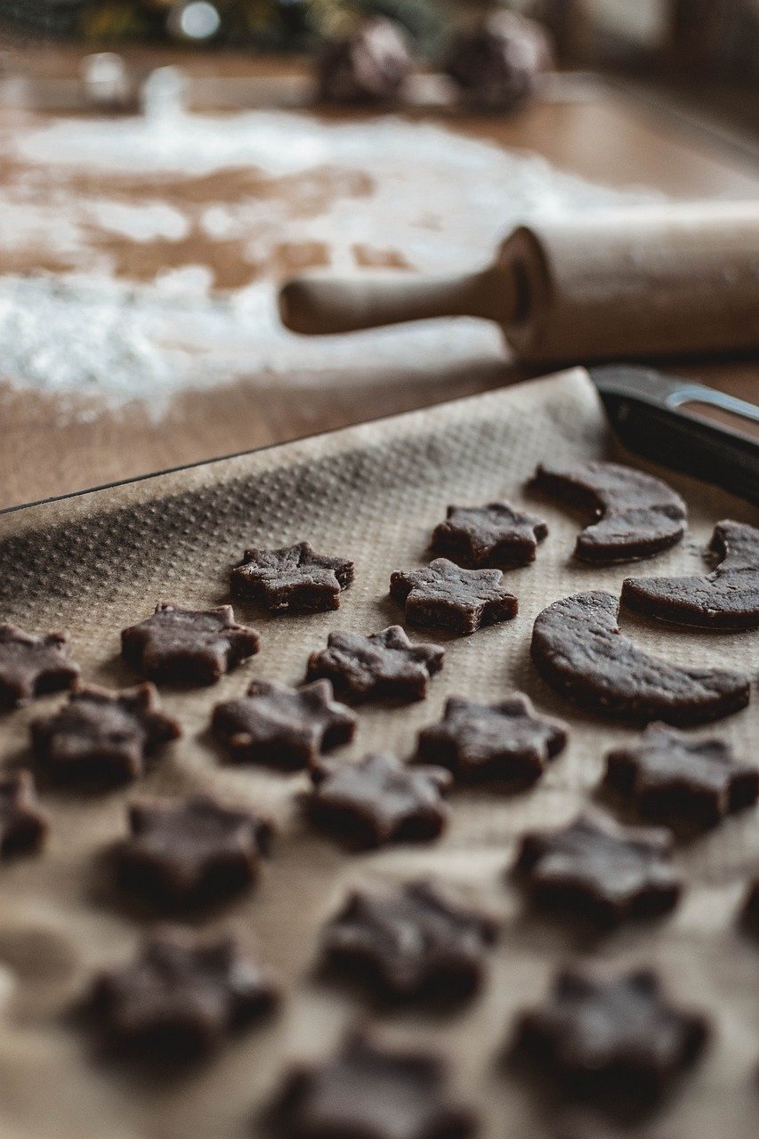 Dark cut-out cookie shapes on parchment with a rolling pin and flour in the background