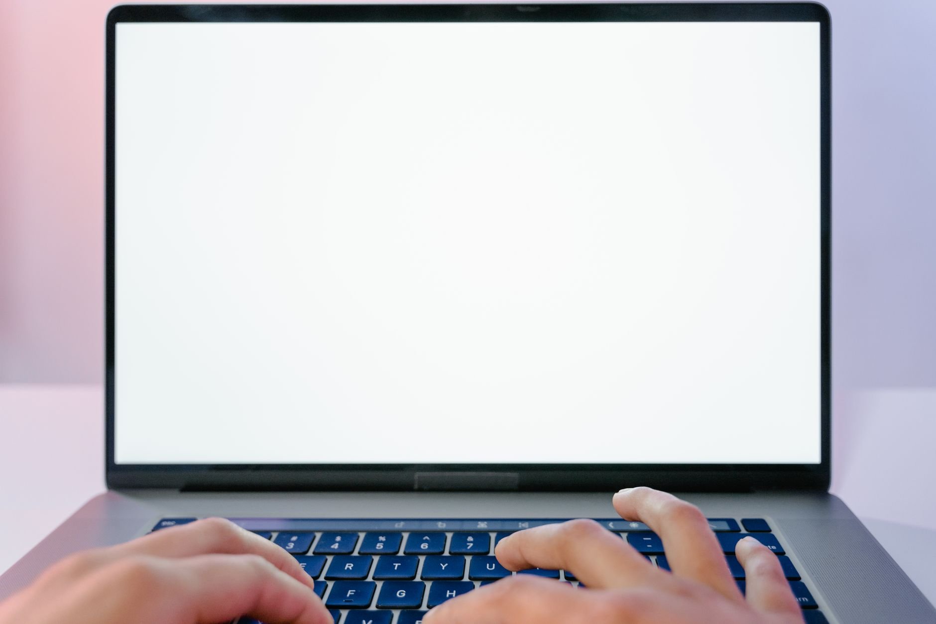 Hands typing on a laptop with a blank white screen against a pink and lavender background