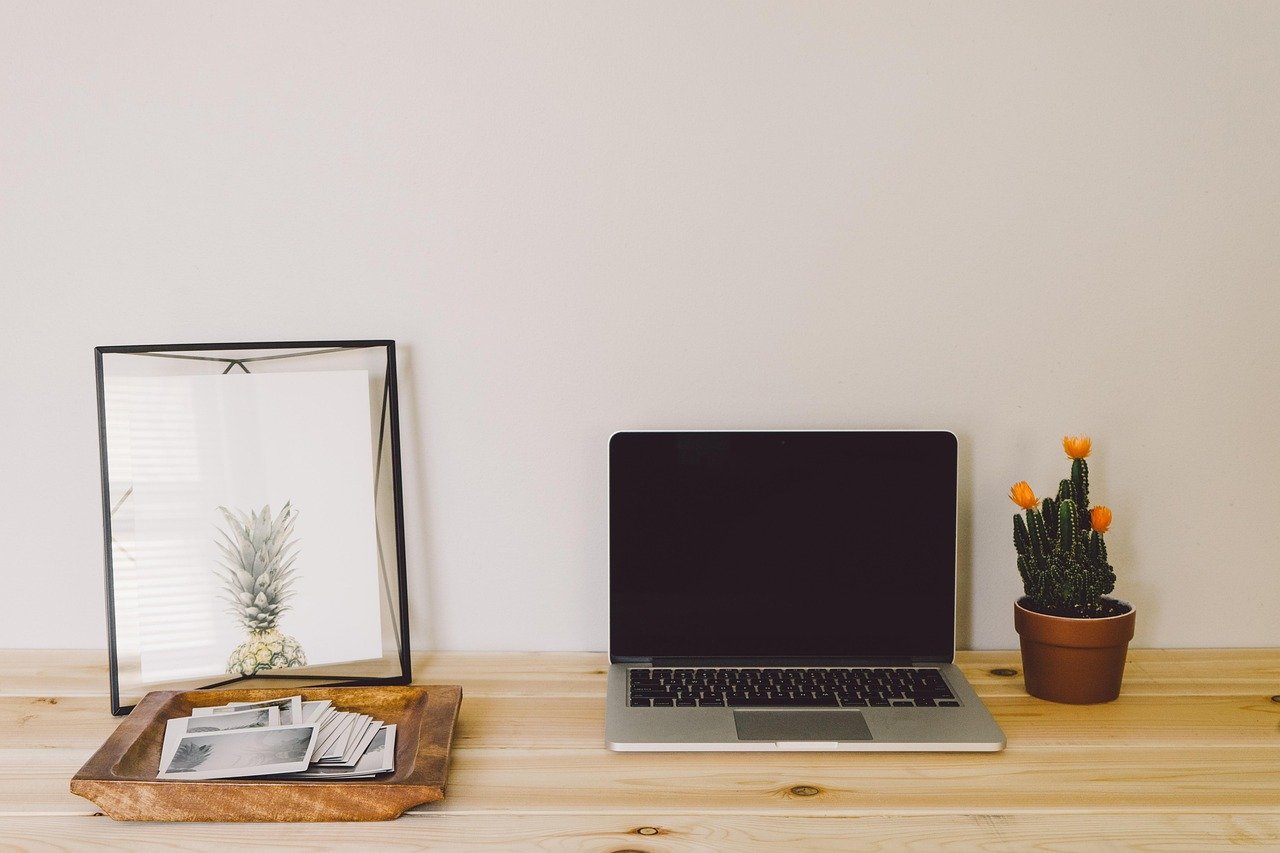 Open silver laptop with a blank, dark screen on a white desk beside a cactus-free workspace
