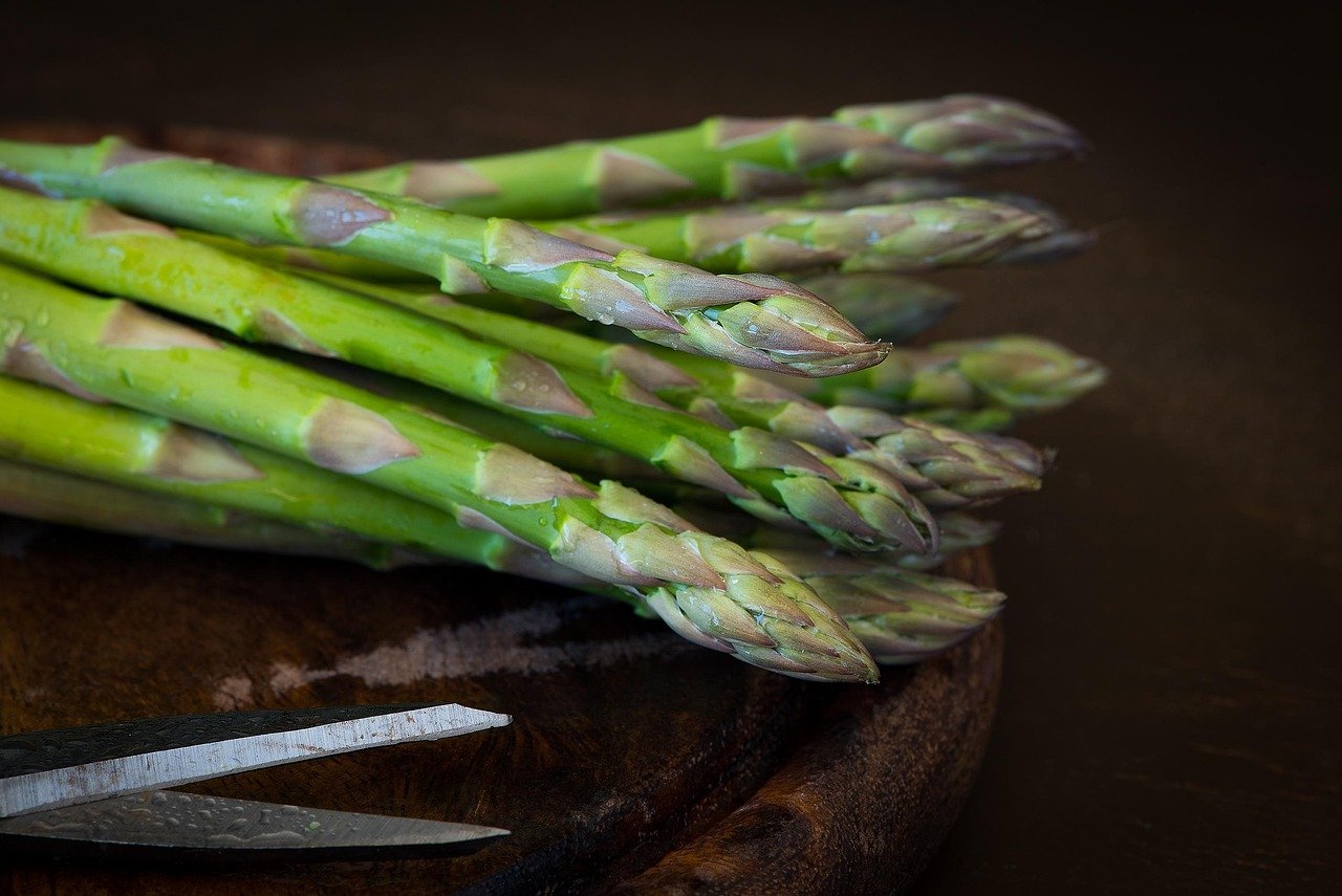 Bundle of green asparagus spears on a wooden board beside a knife