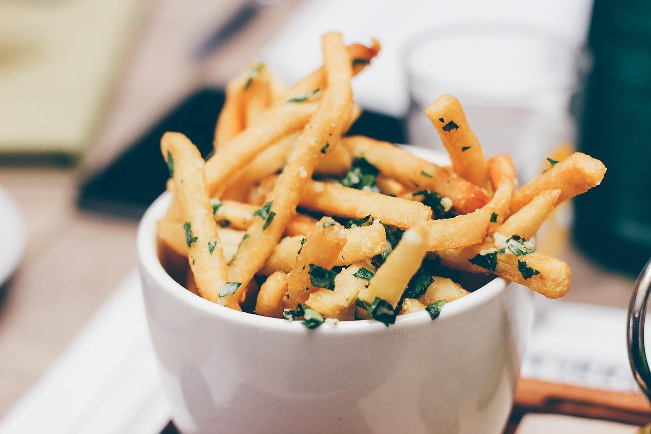 Golden fries with flecks of chopped green herb piled in a white cup on a table