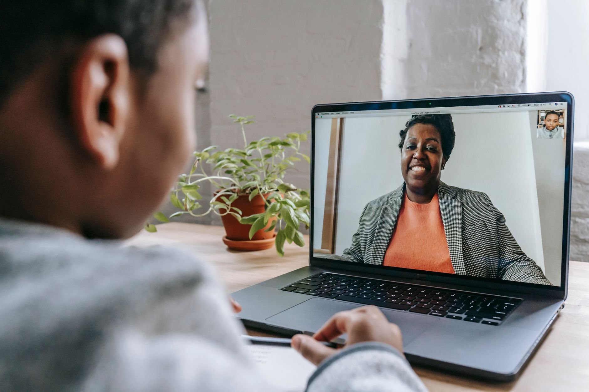 Person at a laptop on a video call with a smiling woman in a grey blazer