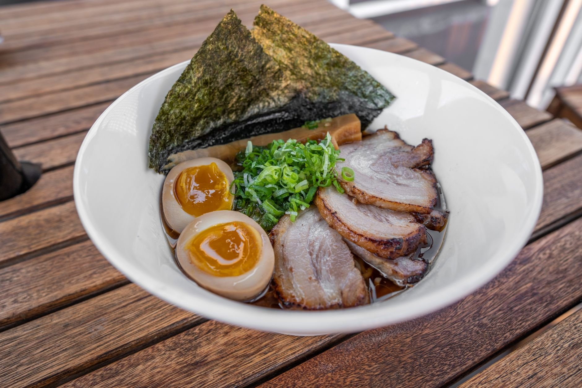 Bowl of ramen with sliced chashu pork, a halved marinated egg, sheets of nori and chopped scallion in a brown broth