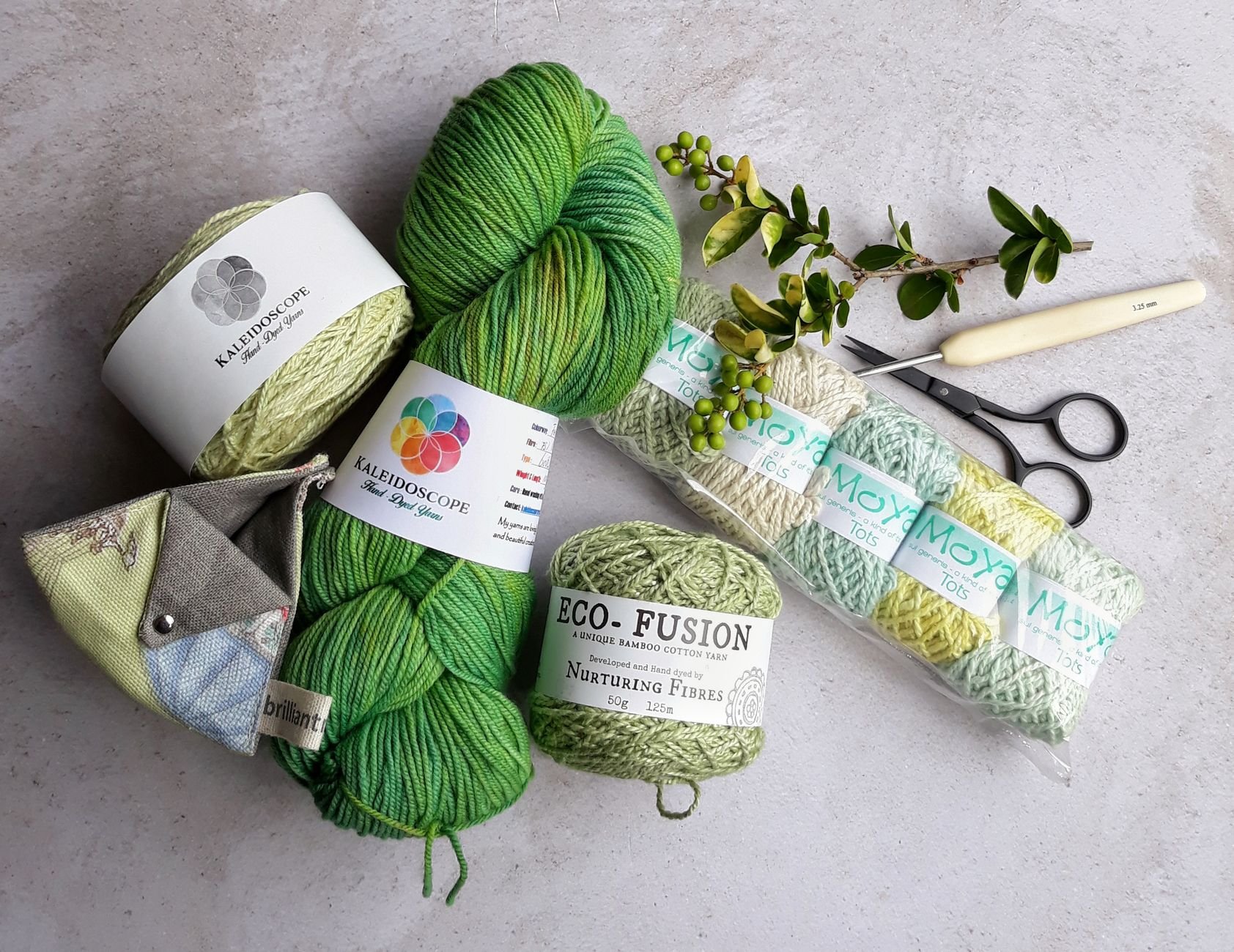 Green yarn skeins, a cream crochet hook, scissors, and a sprig of berries on a light surface