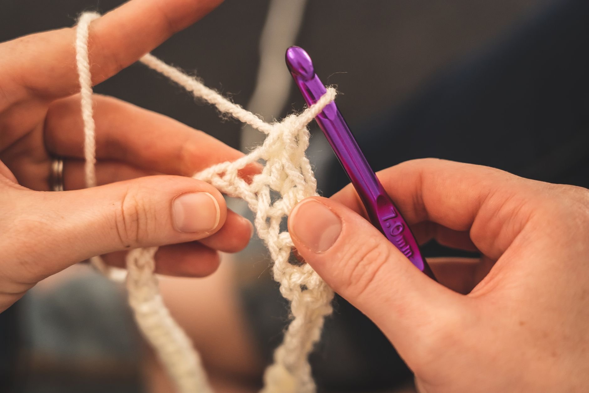 Hands working white cotton yarn with a purple crochet hook on a crocheted edge