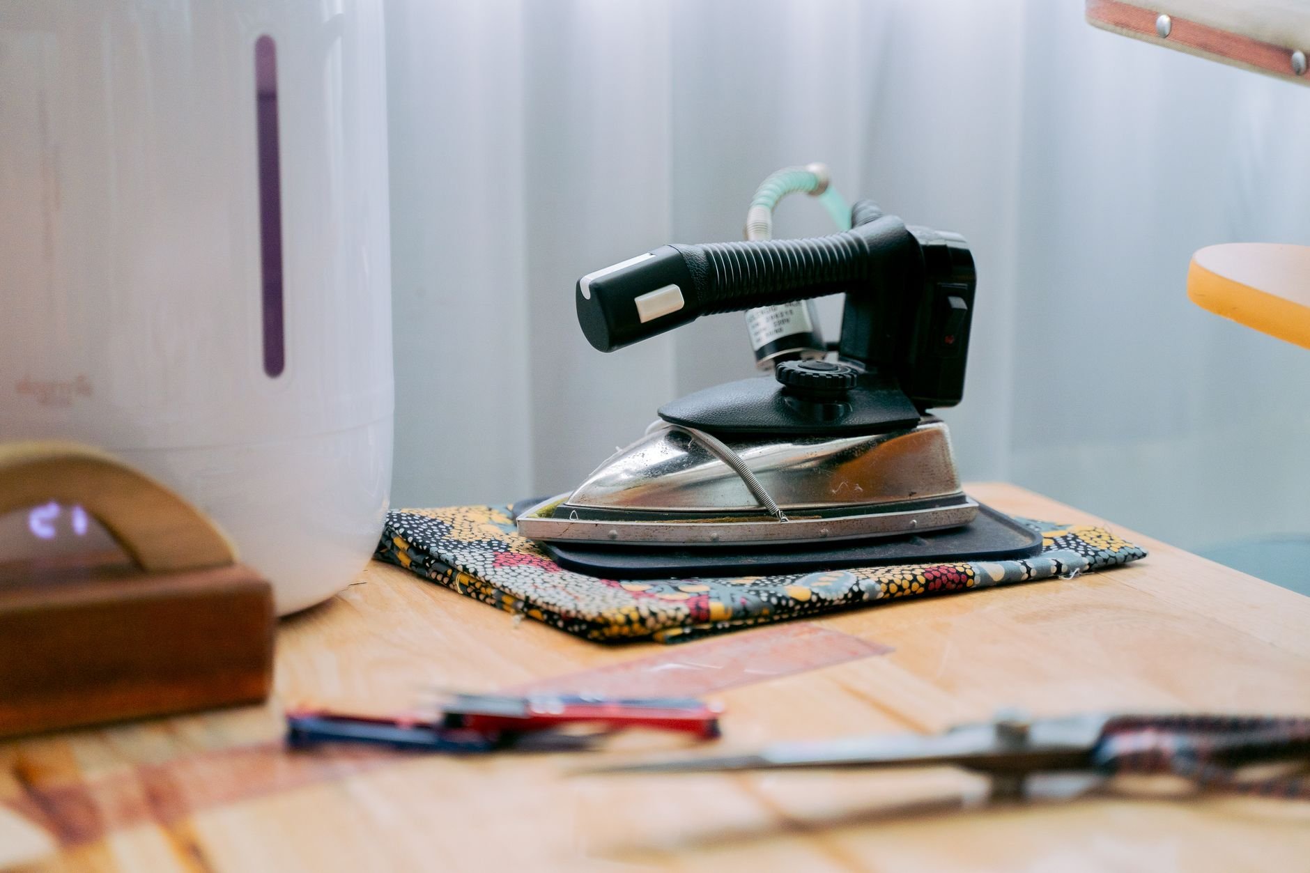 Black iron resting on a small patterned fabric piece on a wooden table, with a pair of scissors in the foreground