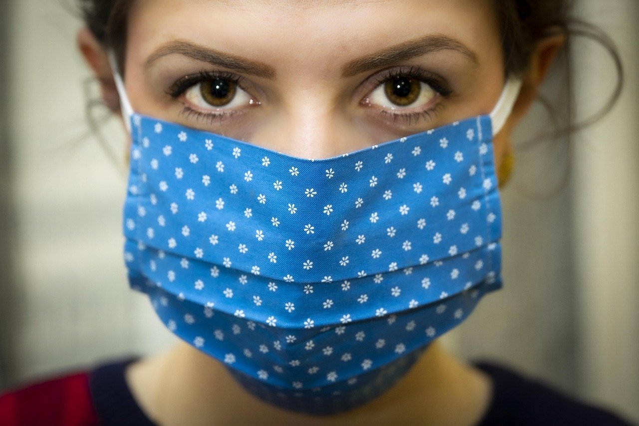 Close-up of a woman with brown eyes wearing a blue fabric face mask with a small white floral print