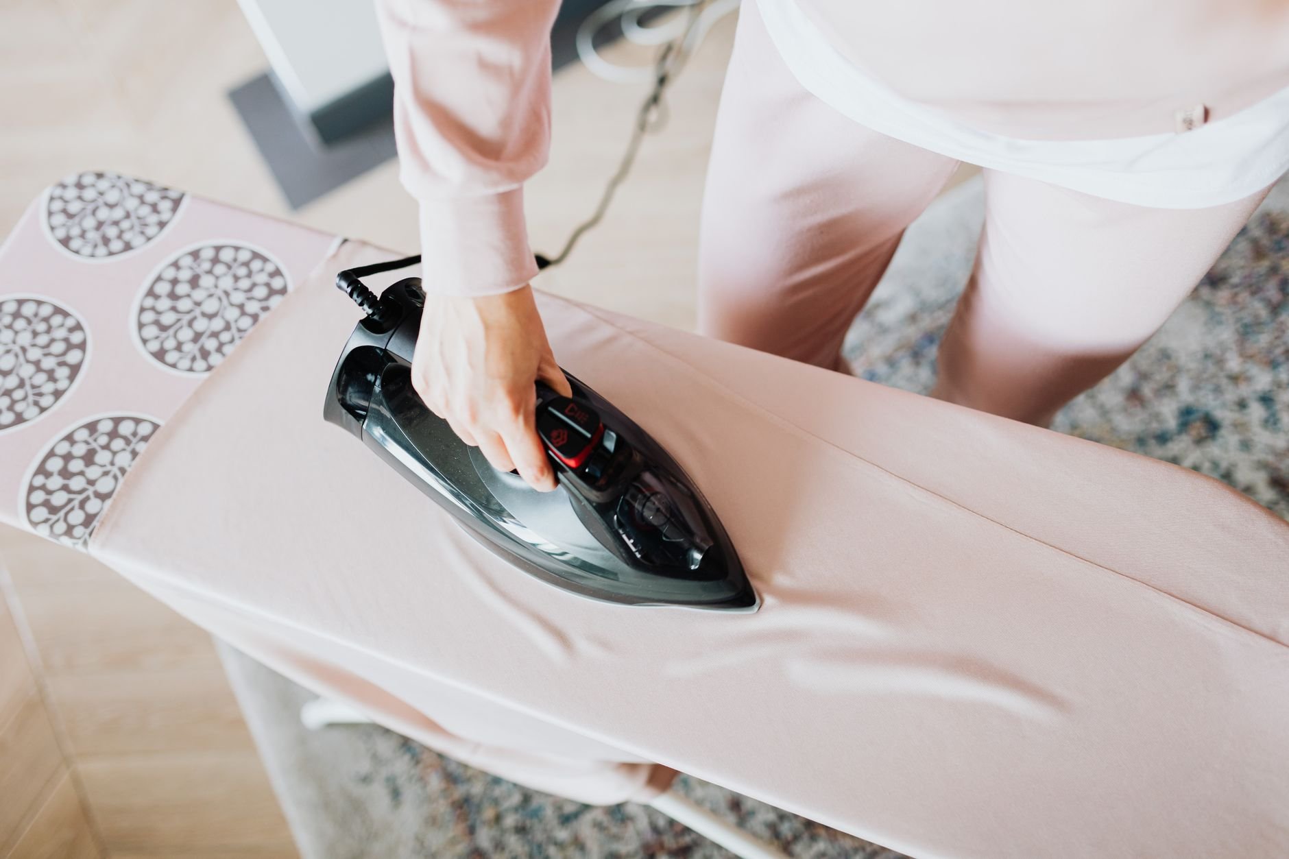 Hand guiding a steam iron over pink fabric laid on a padded ironing board