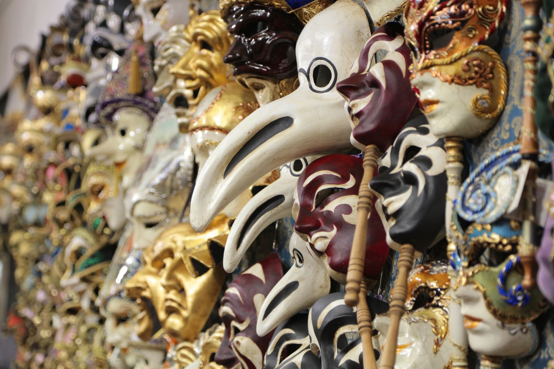 Rows of Venetian masks at a stall, including white beaked masks resembling plague doctor masks alongside gold and painted masks
