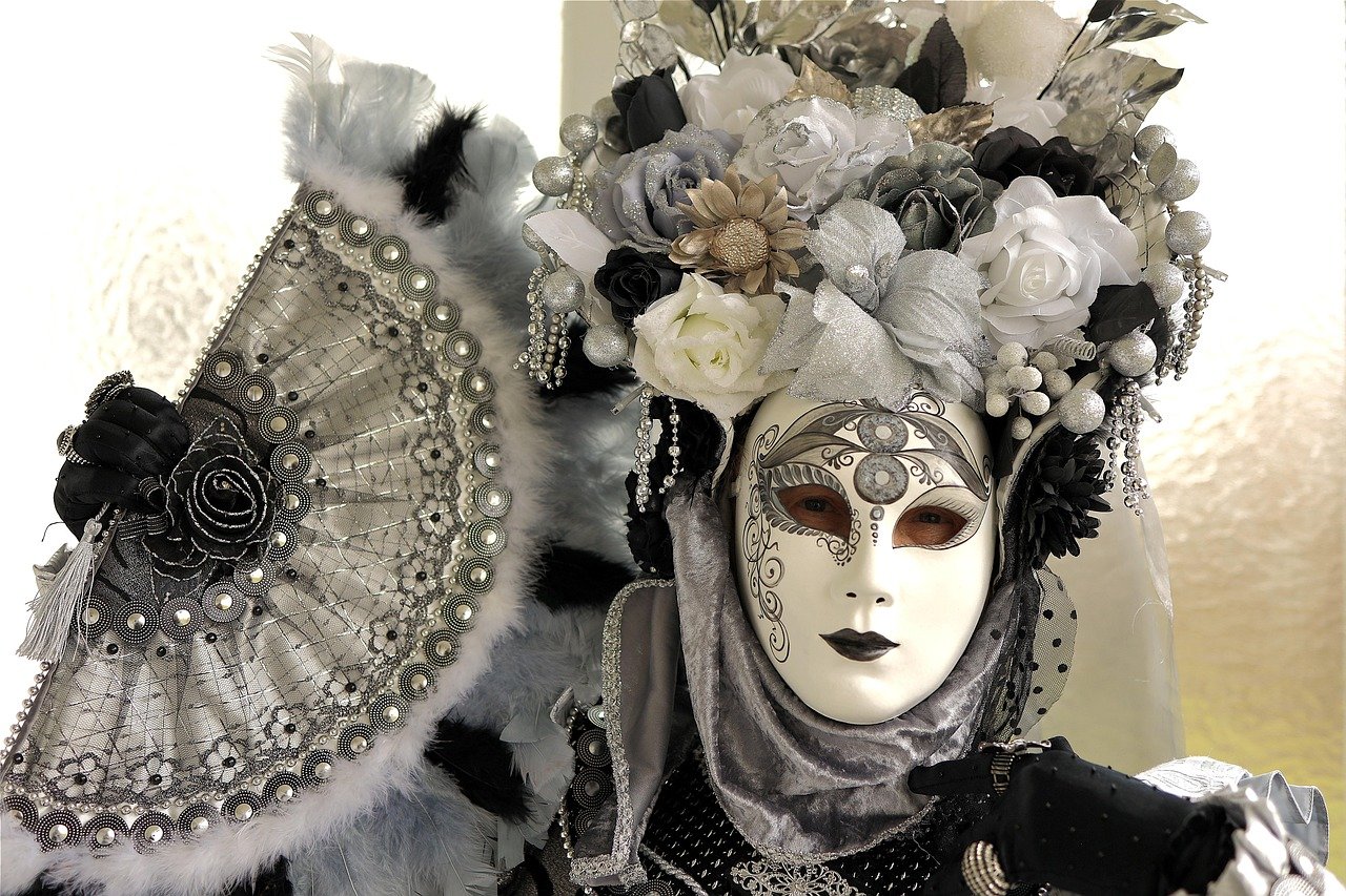 White full-face Venetian-style mask with silver trim and eye openings, worn with a silver flower headdress and a silver lace fan