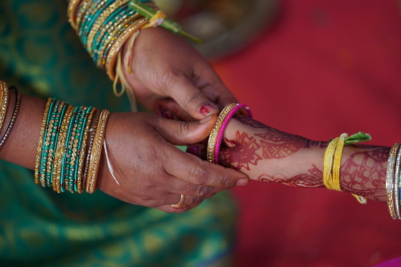 Hands adding green and gold bangles to a wrist decorated with red henna