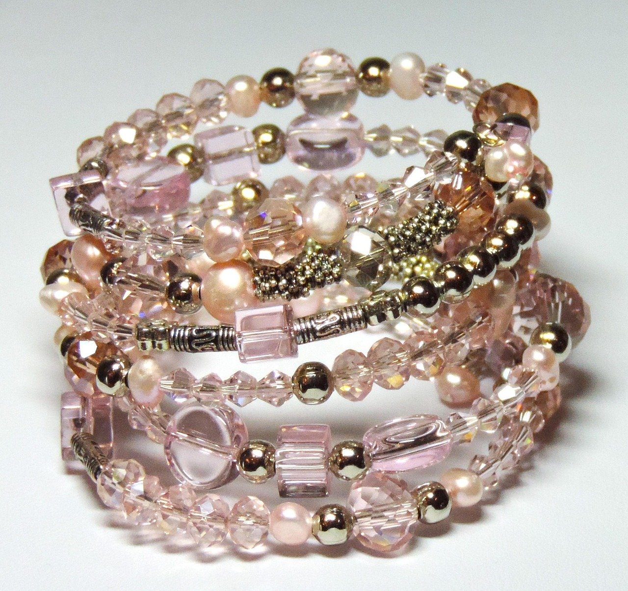 Stack of beaded bracelets with pink crystal, pearl and gold-tone beads on a plain background