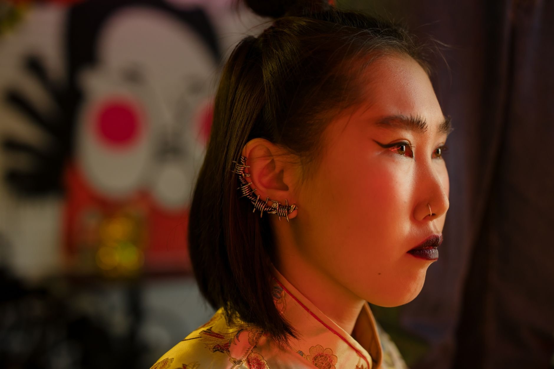 Woman in profile wearing multiple ear cuffs and studded earrings under red lighting