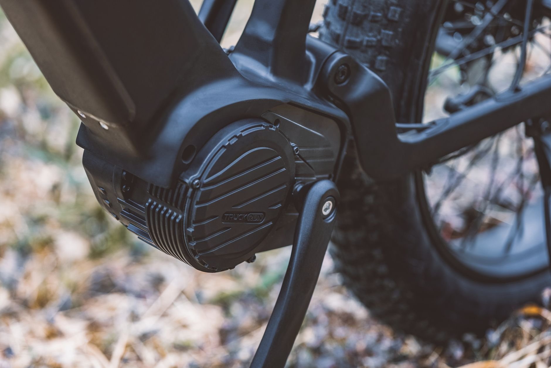 Close view of a black mid-drive motor housing mounted at the bottom bracket of a bicycle with a kickstand