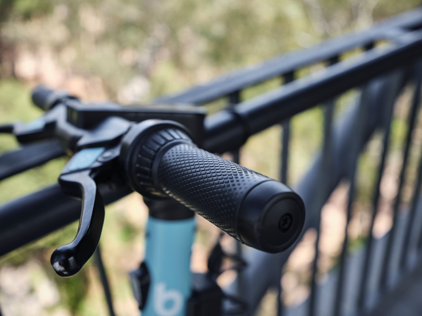 Black twist grip and brake lever on a light blue bicycle handlebar, with a blurred green background