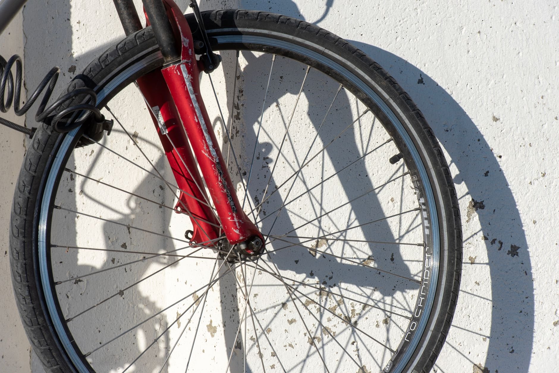 Front wheel with a red fork and dark tyre, with a wheel hub and spokes against a white wall with shadows