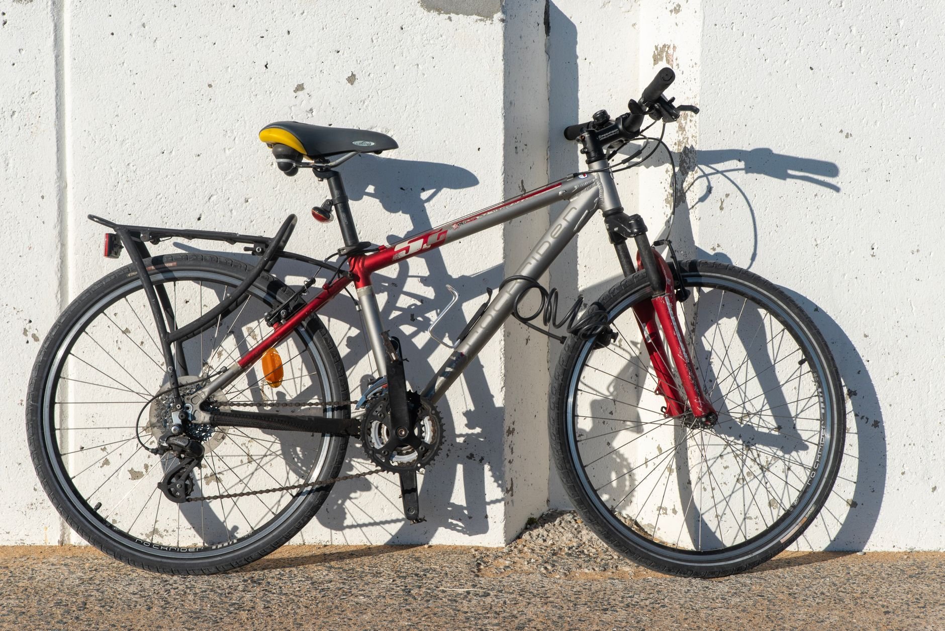 Grey hybrid bicycle with a red fork accent and a rear rack, leaning against a white wall