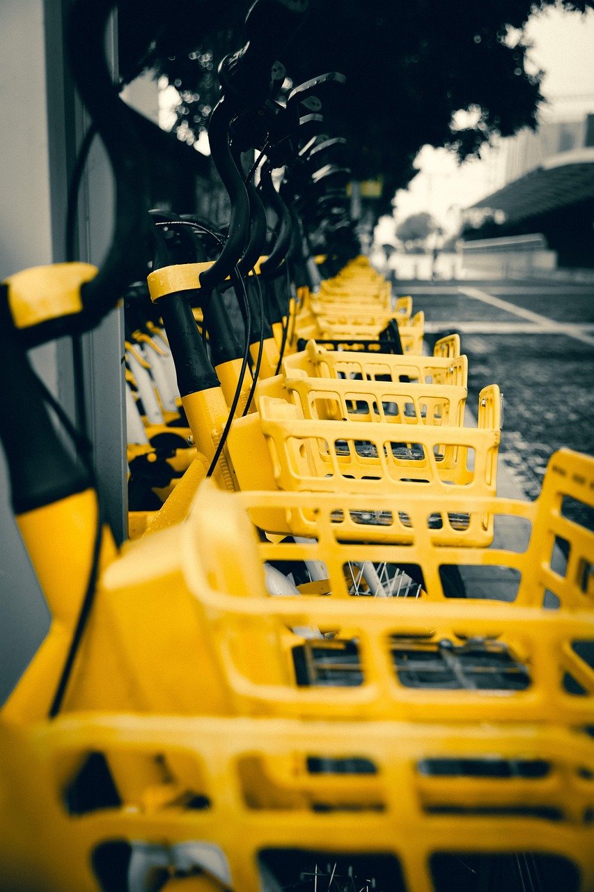 Row of yellow bikes with black handlebars and yellow front baskets docked along a street