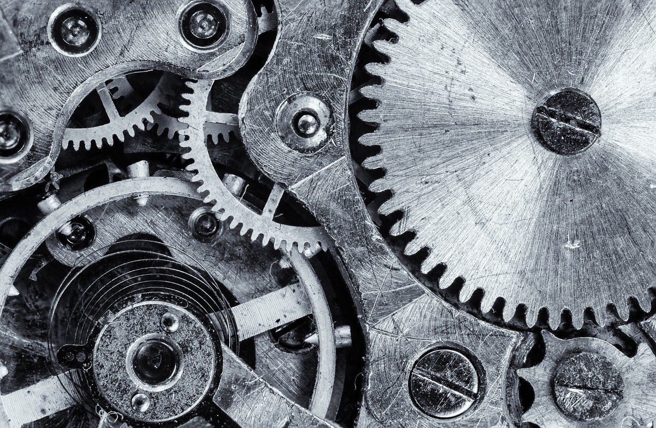 Close-up black-and-white view of interlocking metal gears and wheels with slotted screw heads inside a mechanical movement