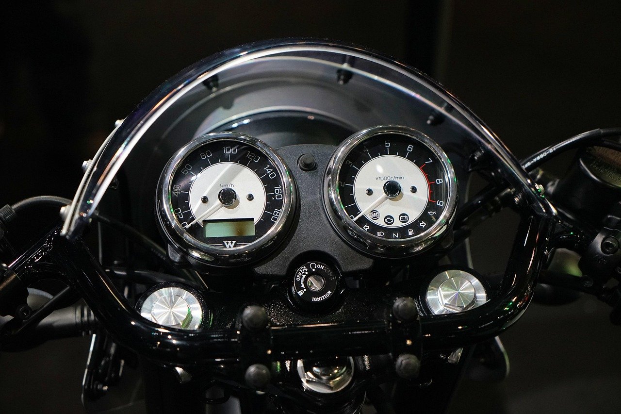Motorcycle handlebar instrument cluster with two round analog gauges, a speedometer and a tachometer, plus a small LCD window on the speedometer face