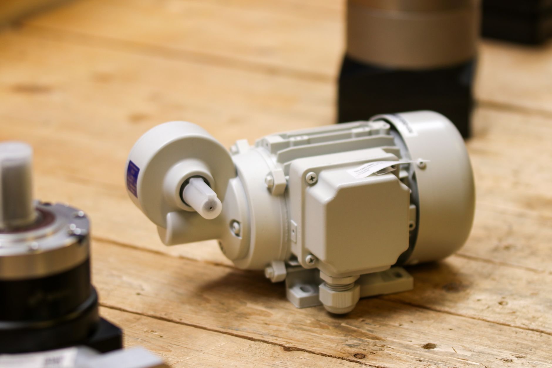 Gray electric motor with an attached gearbox and output shaft lying on a wooden table, with other gearbox components at the edges of the frame