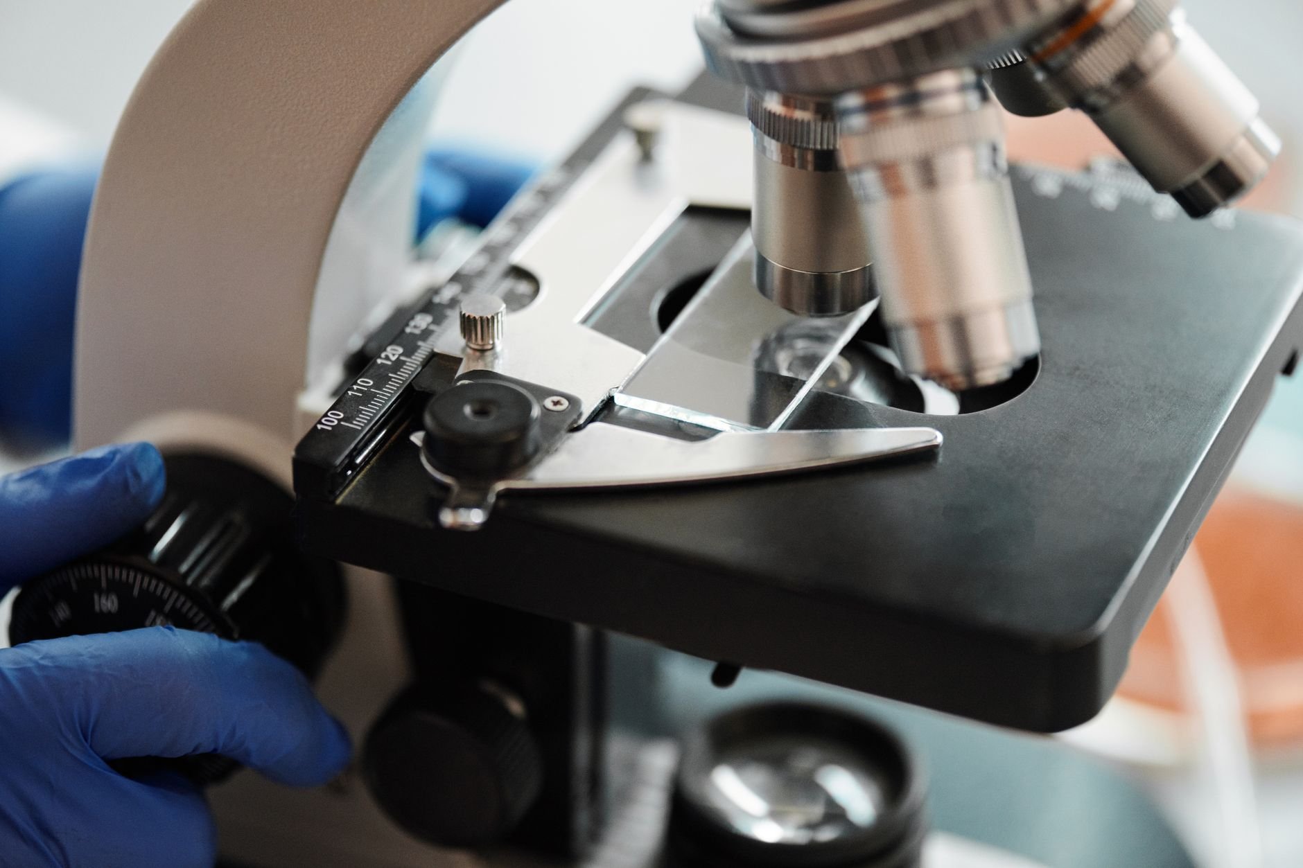 Close-up of a laboratory microscope with a gloved hand adjusting its controls; no tissue specimen or stained slide is visible