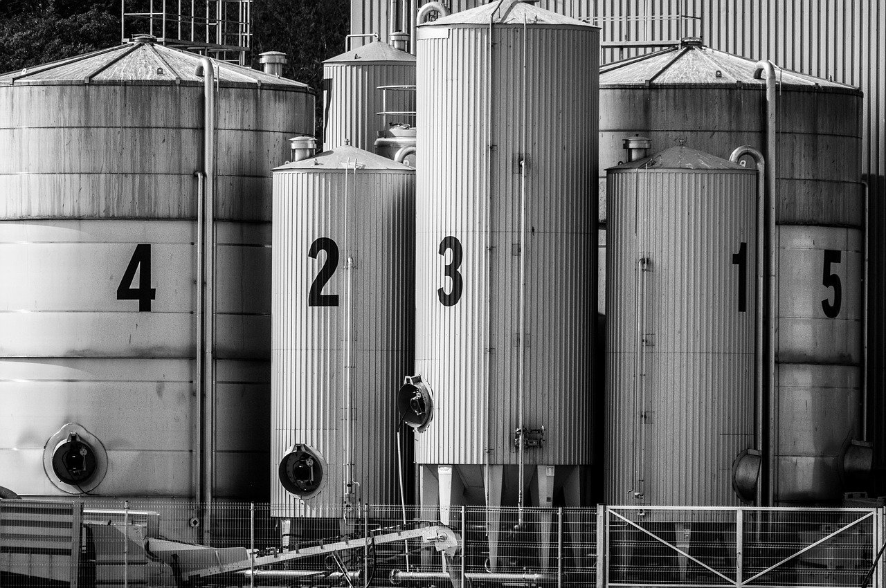 Row of numbered grey corrugated metal silos labeled 1 through 5 beside a metal fence, in black and white