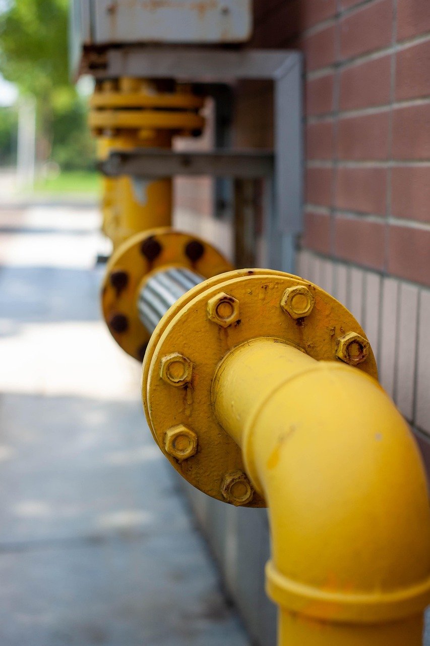 Yellow painted pipe with bolted flanges running along a brick wall outdoors
