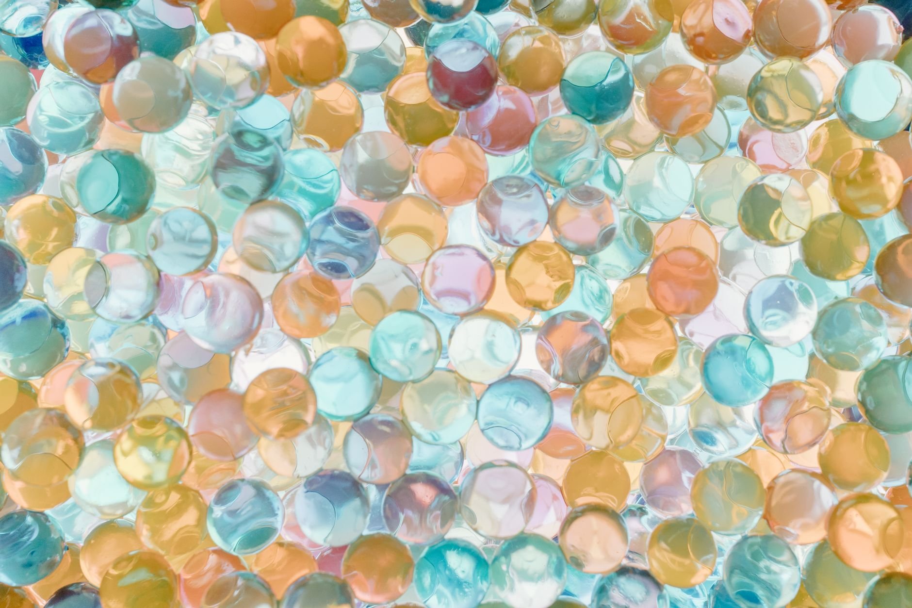 Many translucent beads in blue, teal, amber and pink tones packed together, with light passing through them