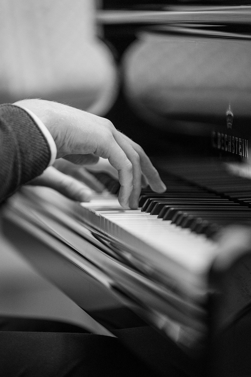 Black-and-white close-up of a hand pressing piano keys, with a blurred piano body behind