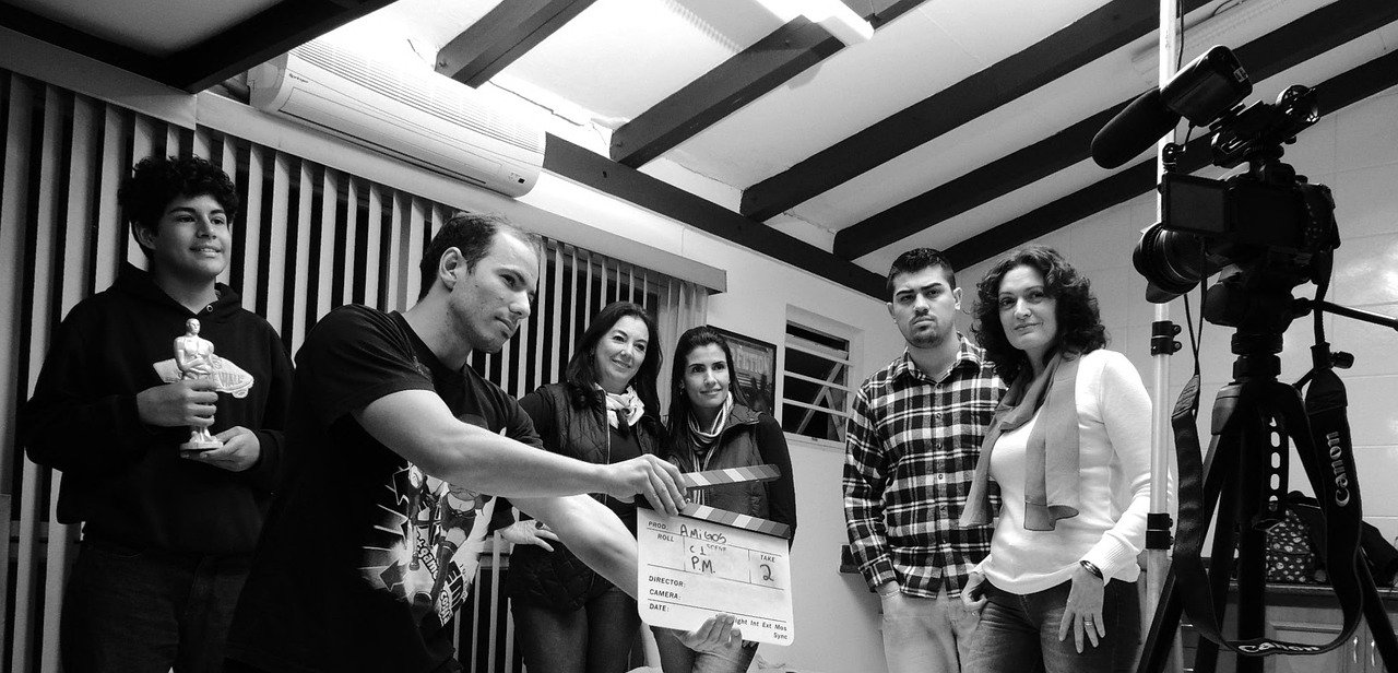 Black-and-white photo of a group of people in a room, a man holding a clapperboard, and a video camera on a tripod at right