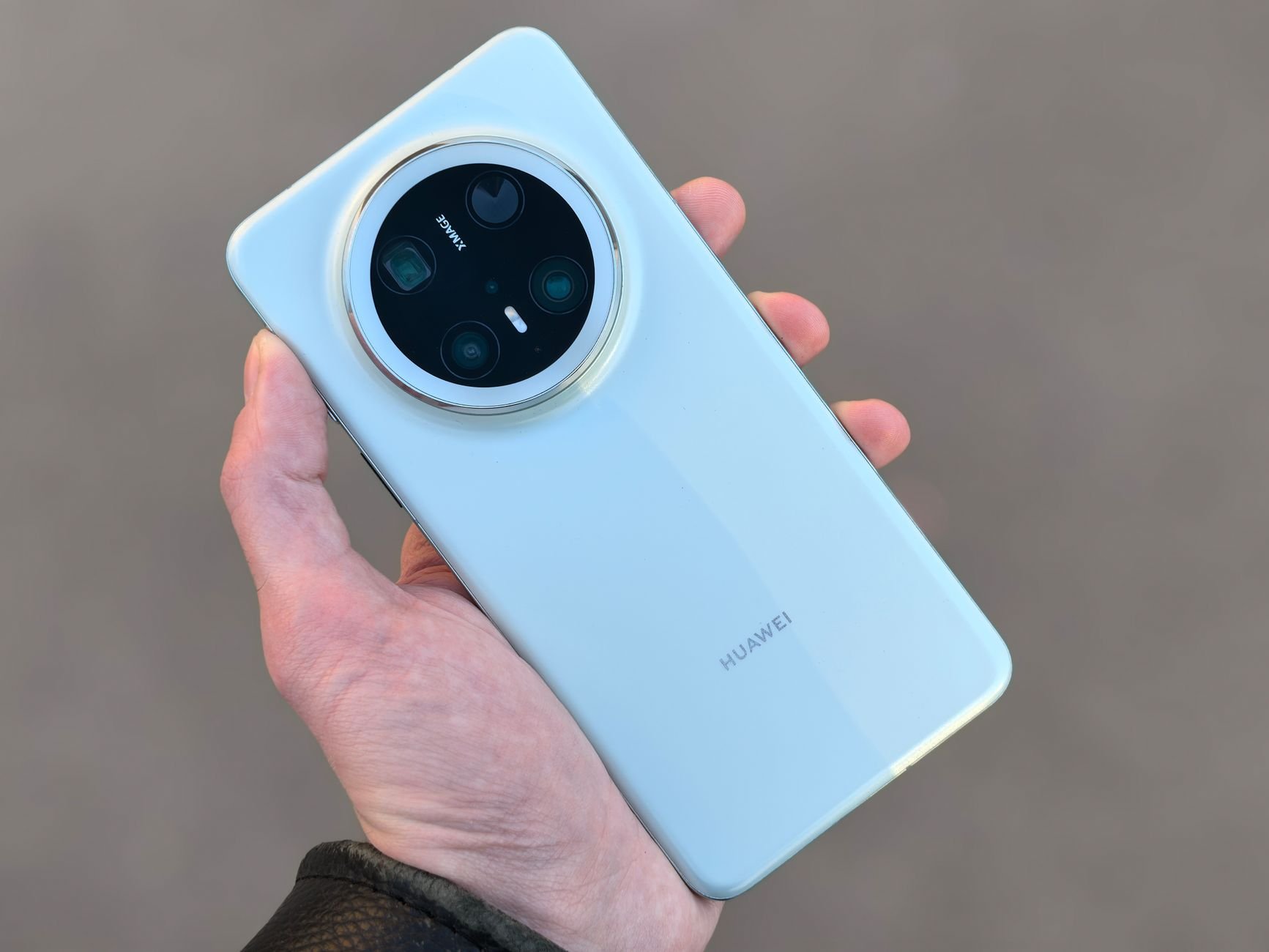 Hand holding a light blue smartphone showing its rear multi-lens camera module with a circular ring around the lenses