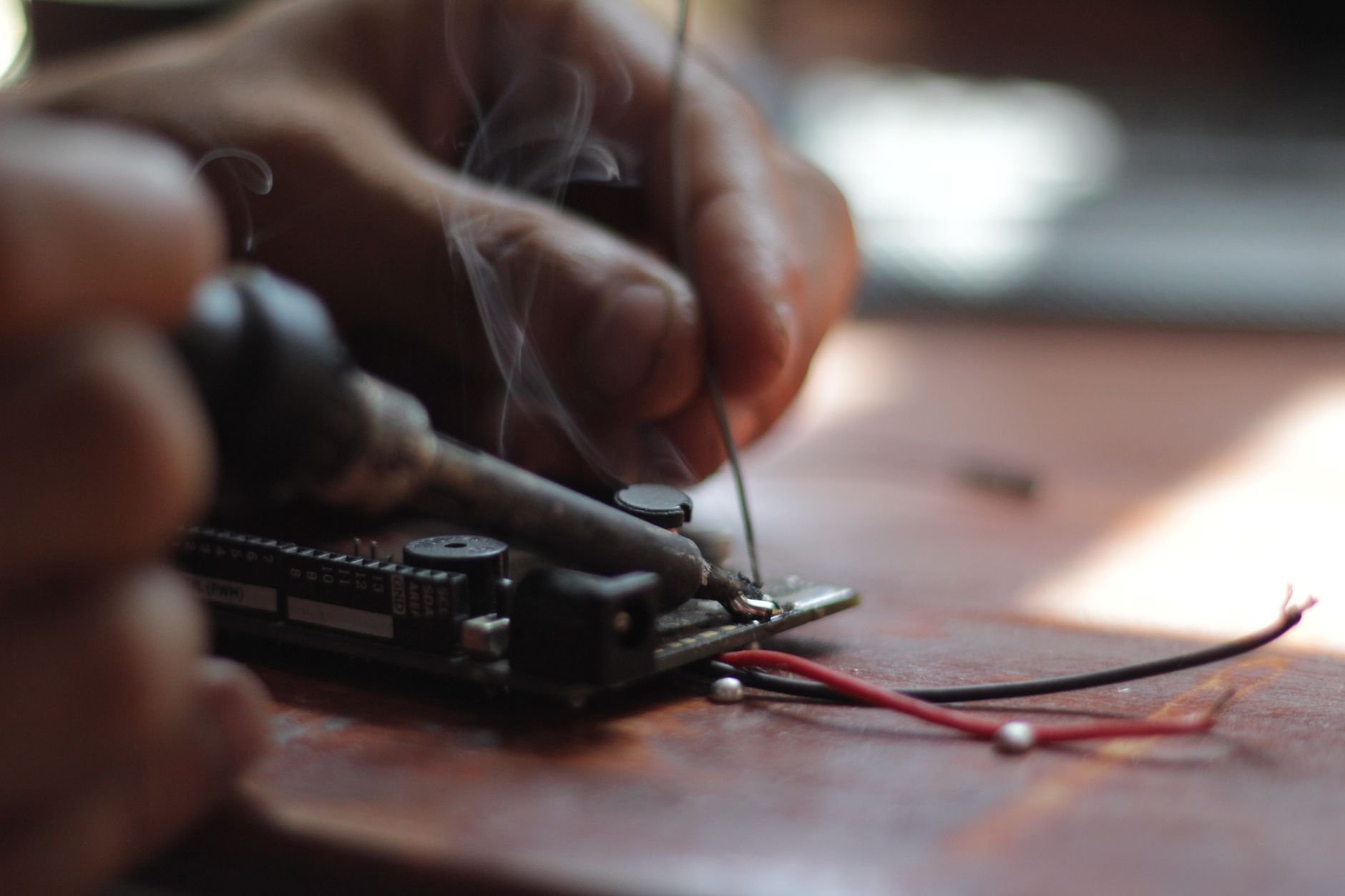 Hands soldering wires onto a small circuit board on a wooden workbench