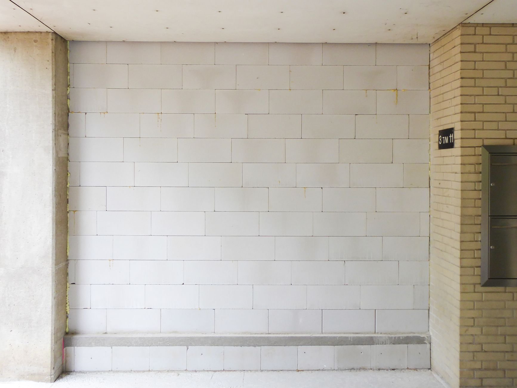 Plain white block wall in a building entrance with a mailbox panel at the right