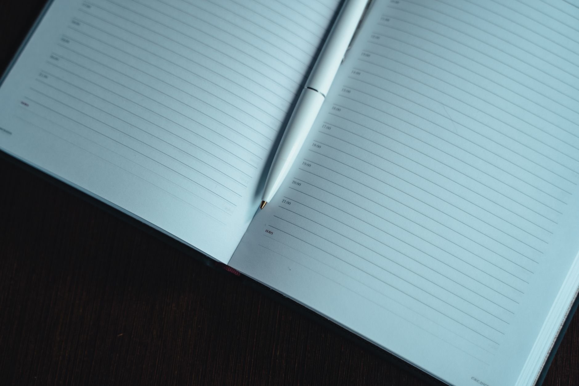 Open blank lined notebook with a white pen on a dark surface