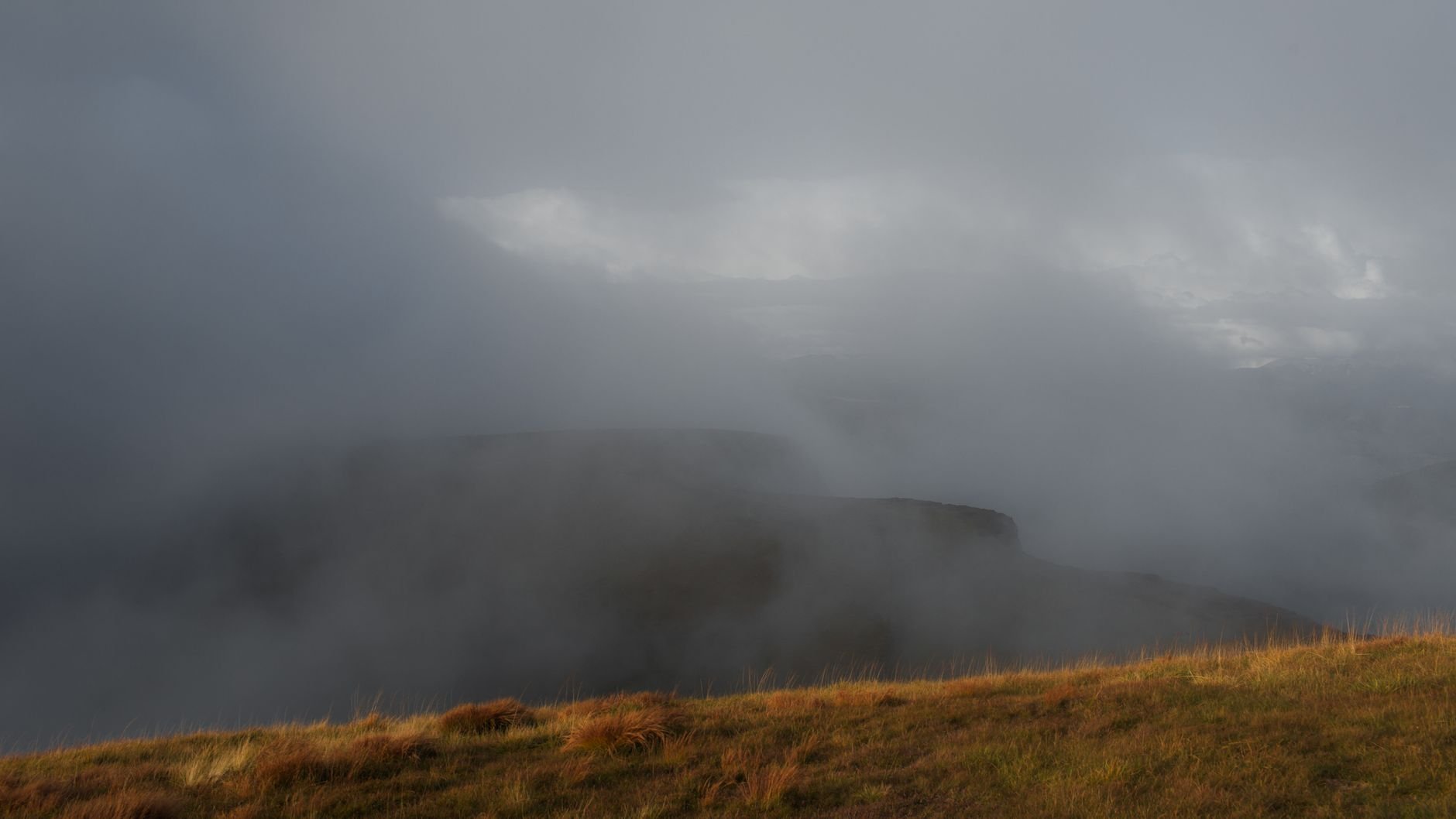 Grey mist and low cloud obscuring a flat-topped hill, with dry grass in the foreground